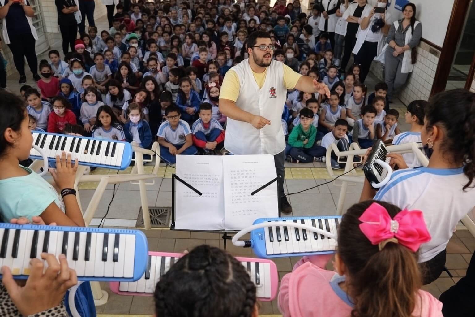Professor regendo alunos com melodicas em escola municipal durante o Dia de Fazer Música | Make Music